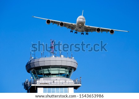 White passenger plane in flight. Aircraft flies over the Air Traffic Control tower (ATC tower).