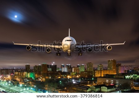 White passenger plane in flight during the night. Aircraft flying in moonlight over the night city. Airplane front view.