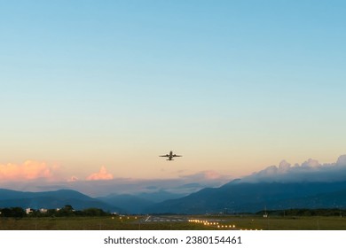 White passenger plane takes off against a beautiful sky with golden clouds and green mountains. Travel by air - Powered by Shutterstock