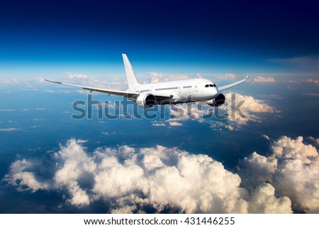 White passenger wide-body airplane. Aircraft is flying in the blue sky over the the clouds.