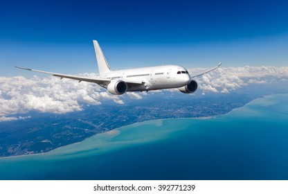 Белый пассажирский широкофюзеляжный самолет. Самолет летит в голубом облачном небе над морем.