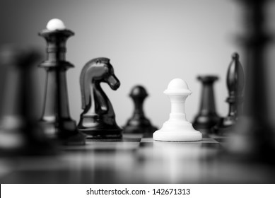 white pawn surrounded by black chess pieces on a chess board