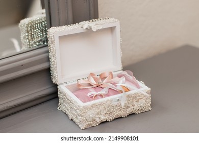 White Pearl Jewelry Box With Wedding Rings On A Gray Dresser