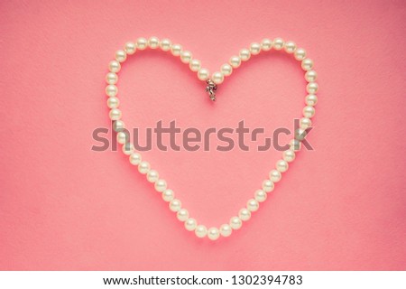 White pearl neckless shaped as heart at pink paper background. Jewelry precious  gift, love, romance and Saint Valentine's Day concept.