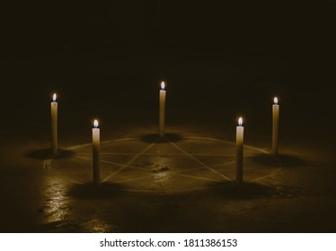 White pentagram symbol on concrete ground. Illuminated with candles. Dark background. Scary, mystical occultism 