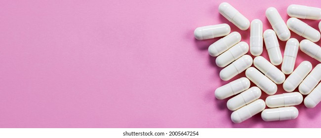 White pharmaceutical pills with colostrum on pink background close-up. Horizontal banner, selective focus, copy space