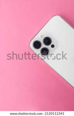 white phone with three cameras on a pink background.