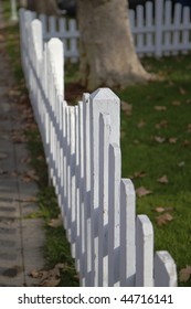 White picket fence in perspective bordered by sidwalk and yard