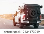 White pickup truck with a black box on the back driving down a highway. Truck has Off-Road package adds skid plates, mud flaps, all-terrain tires, and a suspension lift for better off-road capability.