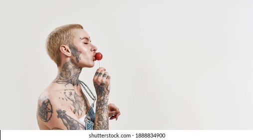 A white pierced woman with a lollipop and a dark-skinned man both tattooed standing next to each other on a white background