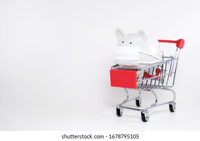 White Piggy Bank Wearing Surgical Mask Inside Mini Supermarket Trolley On White Background With Copy Space. Concept For Healthcare Insurance, Coronavirus Panic Buying, Or Shopping Budgeting.