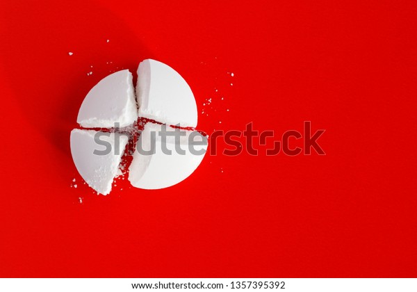White pill broken into four parts on a red\
background. Tablet cut twice. Top\
view
