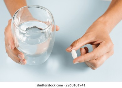 White pill of dietary biologically active supplements and glass of water for daily tablets intake on blue background