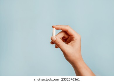 White pill in female hand on blue background, Taking Your Medication