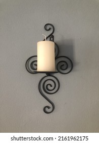 White Pillar Candle On Black Metal Sconce Mounted On A Grey Background