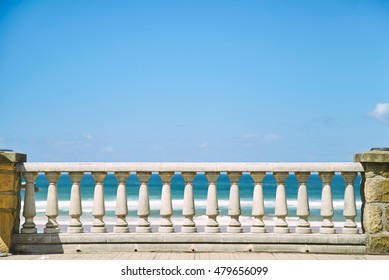 White pillar fence at the seaside promenade between two stone columns on a sunny summer day