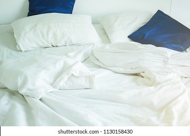 White Pillow And Dark Blue On Bed And With Wrinkle Messy Blanket In Bedroom, From Sleeping In A Long Night, An Unmade Bed In Hotel Bedroom With White Blanket.