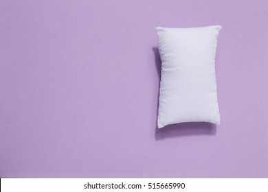 White pillow on soft purple paper background. More sleep equals less stress