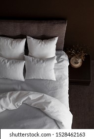 White Pillows, Duvet And Duvet Case On A Bed With Brown Headboard. White Bed Linen On The Sofa. Bedroom With Bed, White Bedding, Nice Posy On The Bedside And Black Wall. Top View.