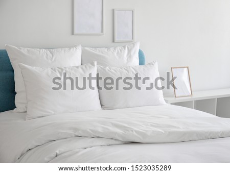 White pillows, duvet and duvet case on a blue bed. White bed linen on a blue sofa. Bedroom with bed and bedding and poster frame mock up on the wall. Left side view.