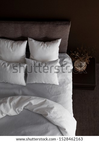 White pillows, duvet and duvet case on a bed with brown headboard. White bed linen on the sofa. Bedroom with bed, white bedding, nice posy on the bedside and black wall. Top view.