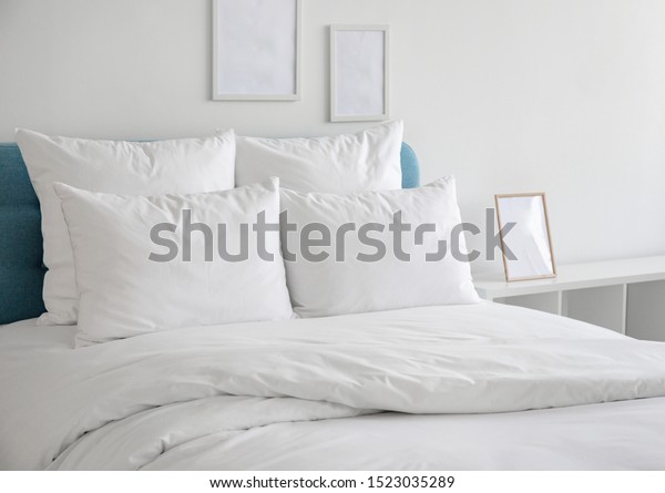 White pillows, duvet and duvet\
case on a blue bed. White bed linen on a blue sofa. Bedroom with\
bed and bedding and poster frame mock up on the wall. Left side\
view.