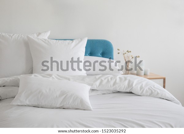 White pillows, duvet and duvet case on a blue bed.\
White bed linen on a blue sofa. Bedroom with bed and bedding. Messy\
bed. Front view.