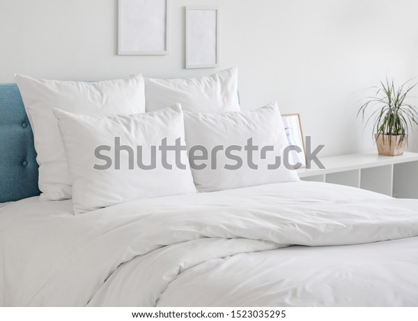 White pillows, duvet and duvet\
case on a blue bed. White bed linen on a blue sofa. Bedroom with\
bed and bedding and poster frame mock up on the wall. Left side\
view.