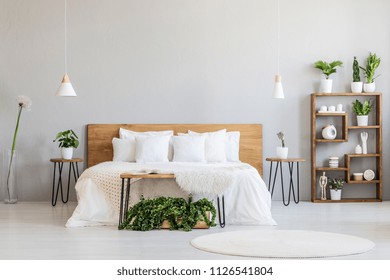 White pillows on wooden bed in minimal bedroom interior with plants and round rug. Real photo