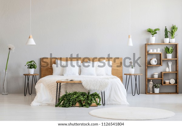 White pillows on wooden bed in\
minimal bedroom interior with plants and round rug. Real\
photo