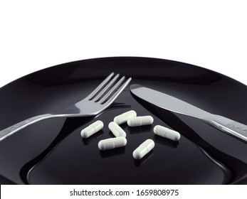 White Pills Capsules On Black Glossy Plate With Fork And Knife On White Background. Diet, Anorexia, Treatment Concept.                               