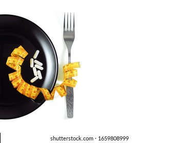 White Pills Capsules On Black Glossy Plate With Fork And Measuring Tape Isolated On White Background Top View. Diet, Anorexia, Treatment Concept. 