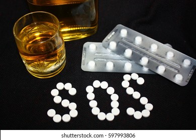 White pills on black background, which forming the word SOS, with glass and bottle of alcohol. Benzodiazepines suicide combination or addiction narcotic concept.