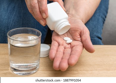 White pills of painkiller or antibiotic for treatment on senior woman hand palm, glass with water, medicines and vitamin supplements concept,close-up view.