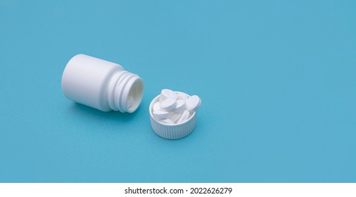 White Pills Are Poured Out Of The Pill Bottle. Pills Are Spilled In A Bottle Cap On A Blue Background. There Is An Empty Space Around The Bottle For Design. Copy Space For Text. Banner For Advertising