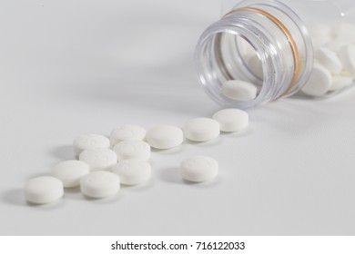 White pills pouring out of the medicine container on a white background