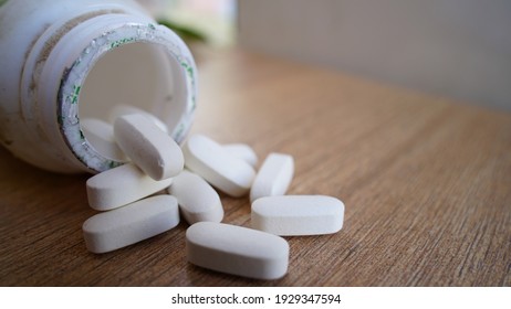 White Pills Spilling Out Of A Bottle On Textured Wooden Background. Heap Of Calcium Pile And Tablets. Medicines, Antibiotic, , Painkiller, Vitamin Supplements Close-up View.