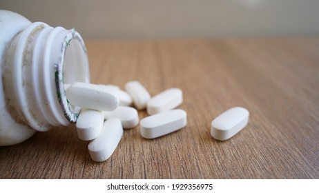 White Pills Spilling Out Of A Bottle On Textured Wooden Background. Heap Of Calcium Pile And Tablets. Medicines, Antibiotic, , Painkiller, Vitamin Supplements Close-up View.