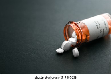White pills spilling out of a toppled bright red orange pill bottle