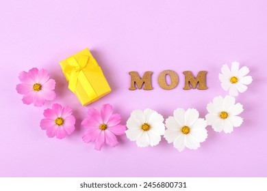 White and pink cosmea flowers, a yellow gift box and the word mama made of wooden letters on a pink background. Mother's Day concept, greeting card - Powered by Shutterstock