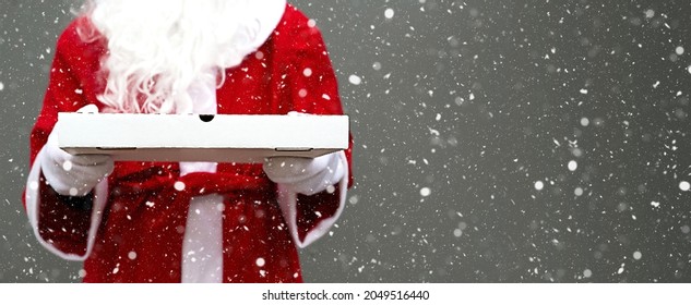 White Pizza Box In The Hands Of Santa Claus In White Mittens, With A Beard, In A Red Coat. Christmas Fast Food Delivery. New Year's Eve Promotion. Work On Public Holidays Catering. Copy Space, Mock Up