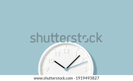 White plain analogue wall clock on trendy pastel blue background. Five past ten oclock. Close up with copy space, time management concept and opening or closing time