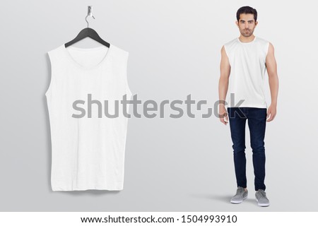 White plan sleeveless shirt on a man male model in black denim jeans pant, isolated, mockup. Hanging white blank sleeveless shirt shirt, against empty wall.