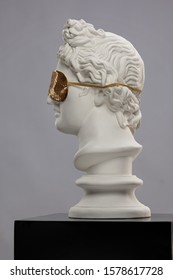 White plaster statue of a bust of Apollo Belvedere in a golden sleep mask covering his face 