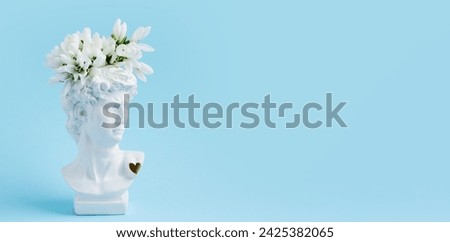 White plaster statue of David's head with snowdrops on pastel blue background. Minimalistic banner with space for text.