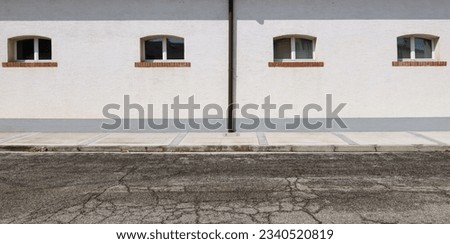 White plaster wall with a row of small windows and gutter in the middle. Concrete sidewalk and street in front. Background for copy space.