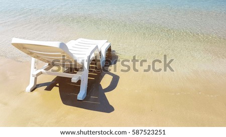 White plastic armchair on the wet beach in hot sunny time with shadow beside the blue sea