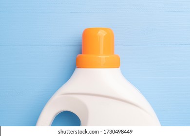 White plastic bottle with a bright orange cap with liquid washing powder or bleach and fabric softener. On a wooden light blue background.