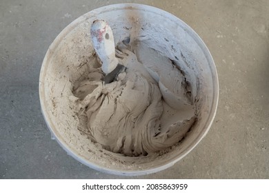 In a white plastic bucket mixed fresh plaster. A trowel is stuck into the mixture. View from above. The concept of room renovation - Shutterstock ID 2085863959