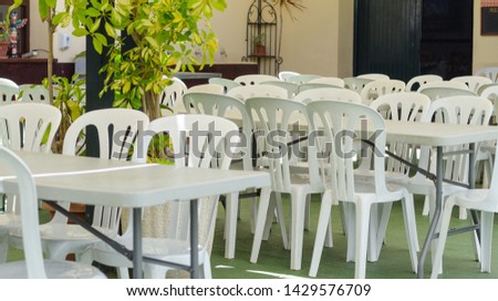 White plastic chairs around tables. ready for a large crowd of people for mass events and parties. The chairs are placed outside under the roof. Andalucia spain, forest park.